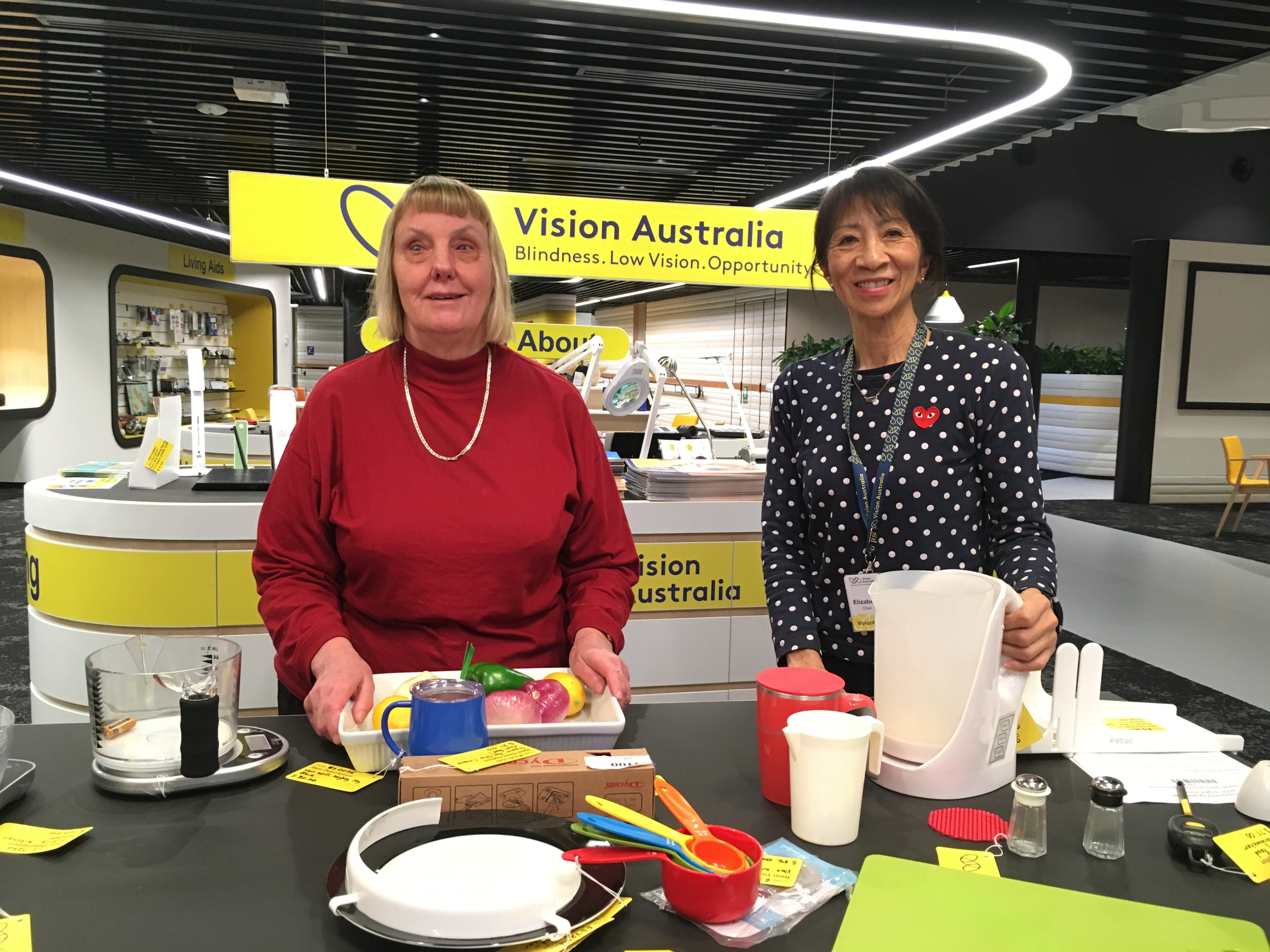 Food for Thought presenters Joy Nuske and Liz Chen in the Vision Australia Store kitchen with various cooking utensils in front of them
