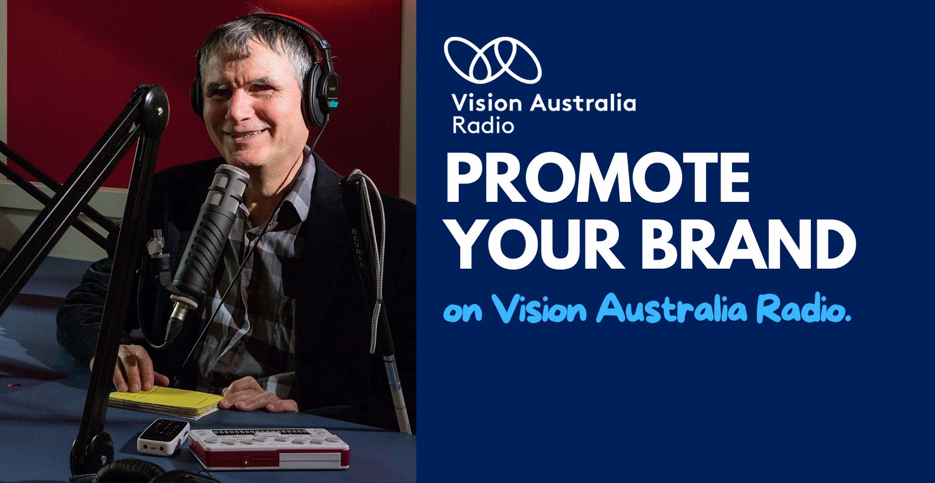 Promote your brand on Vision Australia Radio, Vision Australia Radio logo, man is seated behind a radio desk, wearing headphones, a microphone in front and a white cane rested beside the desk