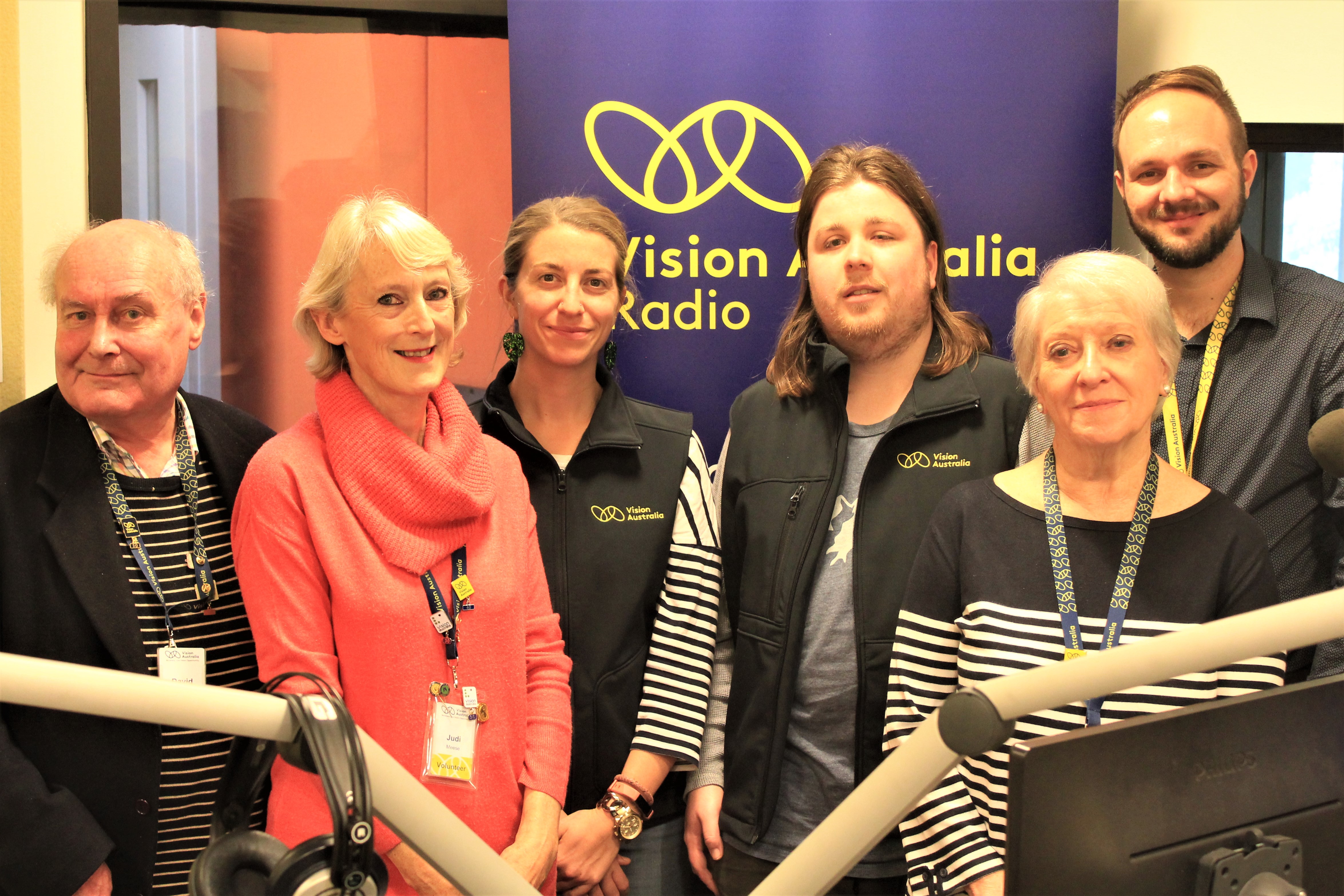 Vision Australia Radio staff and volunteers in the studio with Vision Australia Radio banner in the background