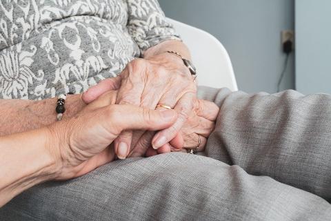 Image shows two pairs of hands of an elderly couple holding one another