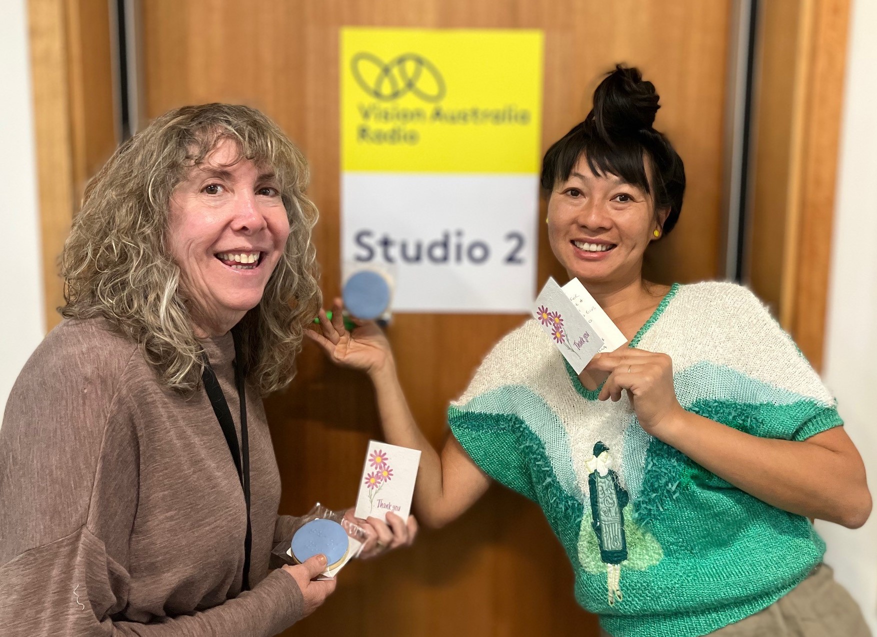 Vision Australia Radio volunteers Donna Olender and Kim-Vu Salamonsen smiling and holding braille cookies